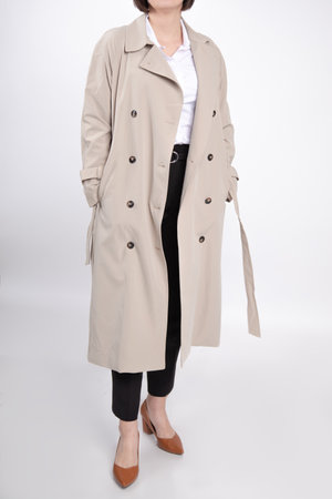 Woman stand in casual beige trench coat, trousers and shoes, crop photo. Female studio portrait, white background.の写真素材