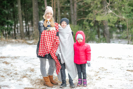 Happy mother, children and spaniel dog in winter forest. Full length photo. Woman warm up under blankets son and puppy.の写真素材