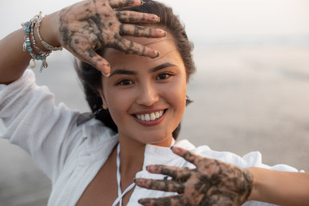 Beautiful young asian woman in white shirt smiles fervently and cheerfully, showing open palms in patterns of wet sand.の写真素材