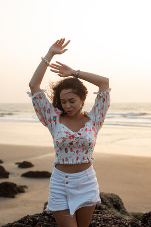 Beautiful young woman stands on seashore against sunset, closing her eyes, completely detached from everything.の写真素材