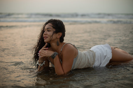 Beautiful young tanned dark-haired woman with long wet hair lies on her stomach in sea water against...