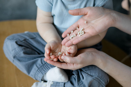 Womens hands pour white flower buds into childrens palms. Development of fine motor skills. Tactile sensations.の写真素材