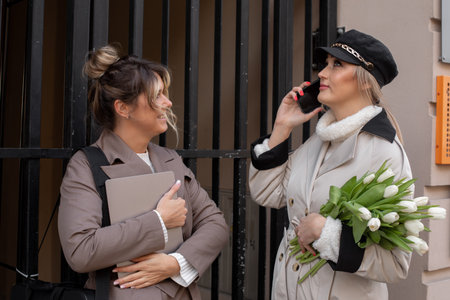 Flower delivery. Two female colleagues in floral business are standing on street against background...