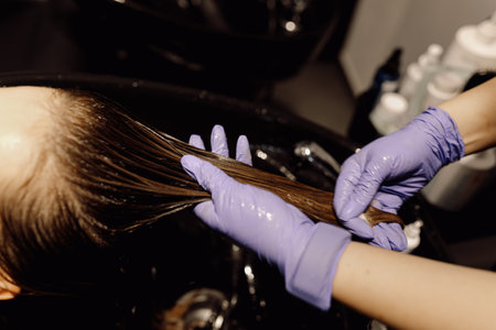 Cropped photo of beautician wearing blue gloves washing long dark hair of client in professional basin in beauty salon.の写真素材