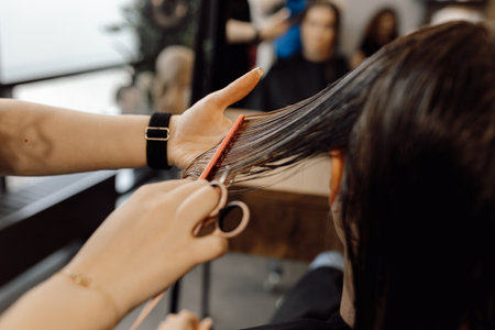 Cropped photo of woman beautician making hairstyle brush long wet hair with pink comb, holding scissors in beauty salon.の写真素材