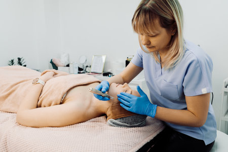 Female doctor applying dermapen device for relaxed woman patient, lying on couch in spa clinic on beauty proceduresの写真素材