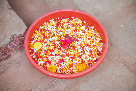 Red bowl with hand washing water on floor, from above view. Bright flower petals soaking in water....