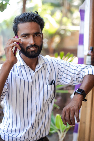 Attractive Indian man in white striped shirt is talking on phone and looking at camera. Modern technologies. Lifestyle.の写真素材