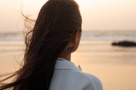 Closeup rearview headshot of brunette long haired woman in in white shirt contemplate at seawater horizon and sunset skyの写真素材
