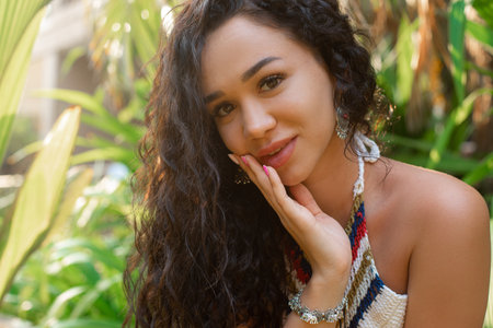 Close up portrait sensual, alluring brunette curly woman in traditional bracelet and earrings among plant arrangementの写真素材
