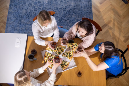 Top view of middle-aged women relatives sitting at table, talking, holding pieces of pizza, glasses...