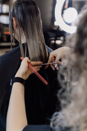Cropped photo of woman hairstylist making hairstyle cutting tips of long dark hair, holding...