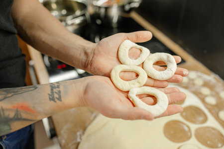 Cropped photo of man holding raw round doughnuts donuts in hands for frying in hot oil in metal pan in kitchen at home.の写真素材