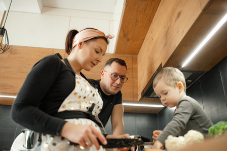 Portrait of family of young woman, little son and man cooking soup in kitchen at home. Mother cutting with black knife.の写真素材