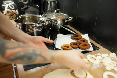 Cropped photo of man taking raw yeast doughnuts donuts for frying in hot oil in metal pan near skimmer on black cooker.の写真素材