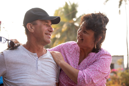 Portrait of smiling tanned middle-aged couple of woman and man sitting closely outside, embracing...