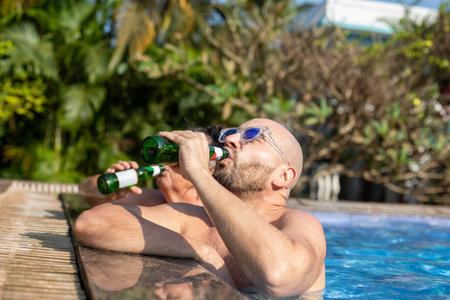 Side view of handsome young bald bearded handsome man wearing blue sunglasses, standing in swimming...
