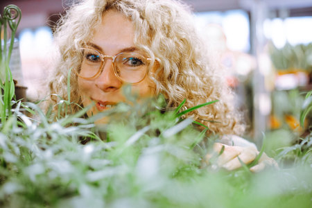 Portrait of happy blonde in glasses with curly luxurious hair in afternoon in garden center among...