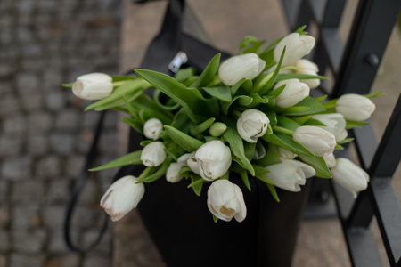 Portrait of black bag with white flowers standing by the sidewalk of cement near black fence . Spring mood.の写真素材