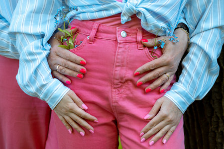 Young lady in pink skinny jeans and blue shirt. Blue fowers in pants pocket. Hands lie beautifully on stylish jeans.の写真素材