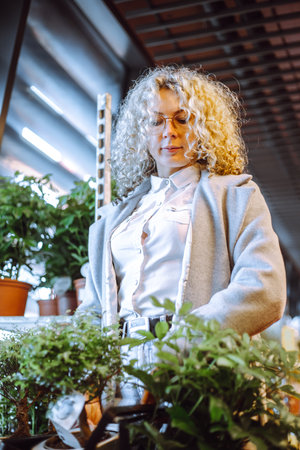 Portrait of attractive blonde with curly hair choosing plants forwinter garden in garden center. Wonderful gift.の写真素材