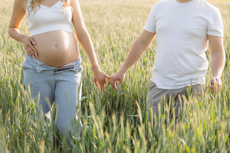 Unrecognizable married couple during their wifes pregnancy enjoys walk in nature on summer day holding hands. Family.の写真素材