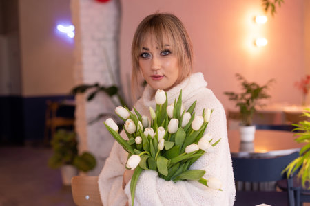 Portrait of a young girl with blond hair holding white tulips in room inside where is full length...