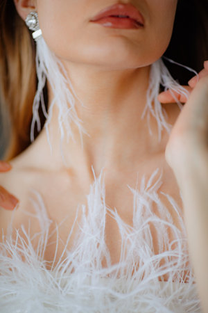 Close up of collarbone of young lady wearing wedding attire decorated with fluffy feathers and tassel earrings in ears.の素材 [FY310207941580]