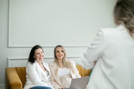 Female team discussing work ins in home office. Brunette and preggers lady sitting on sofa and listening to colleague.の写真素材