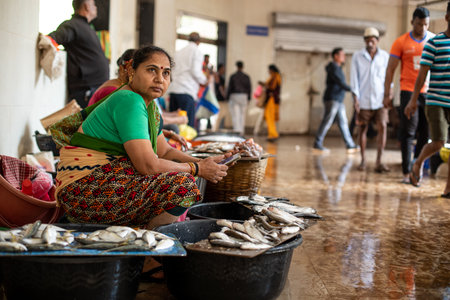 Goa, India, February 2023. Side view of middle-aged woman sitting near seafood stalls, selling and cleaning fresh fish.のeditorial素材