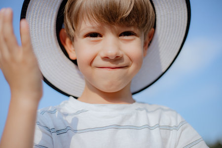 Close-up portrait of happy boy in white panama hat on summer day against sky. Holidays, recreation.の写真素材