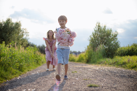Son with bouquet of peonies and laughing mother are photographed on summer day in countryside.の写真素材