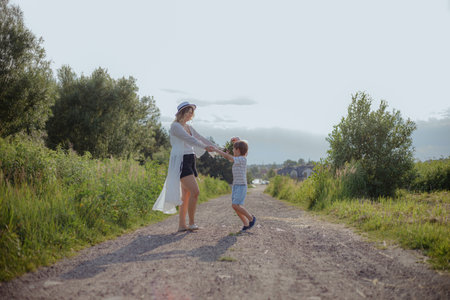Mom, son are happy together. Having fun,mother and son are spinning holding hands on rural road .の写真素材