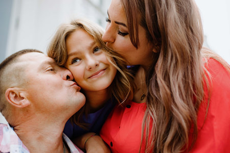 Close-up of happy charming girl is happy, she is kissed from both sides by mom and dad on day.の写真素材