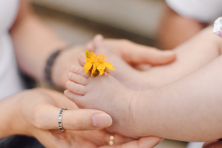 Close-up of small childs foot with fingers with flower inserted, which is held by parental hands.の写真素材