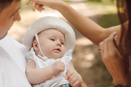 Charming little girl in white panama hat 4-6 months in arms of her father on summer day for walk.