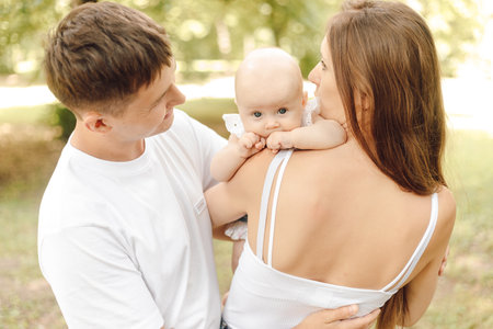 Marital and parental love and tenderness. Mom, dad and newborn baby in park on sunny summer day.の写真素材
