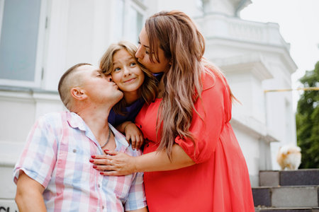 Happy charming girl is happy, she is kissed from both sides by mom and dad on summer day in park.の写真素材