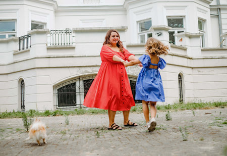 Harmonious happy family.Mom and daughter in bright dresses are spinning having fun on summer day.の写真素材