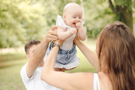 Close-up of little newborn girl who is held high by her father and mother on summer day in nature.