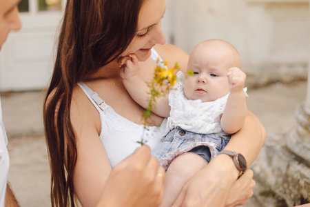 Smiling mother holds her charming little daughter, unrecognizable dad gives yellow flower to child.の写真素材
