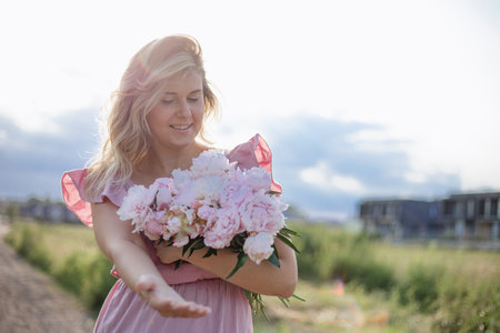 Charming woman with disheveled hair in summer sundress with bouquet of peonies on summer day .の写真素材