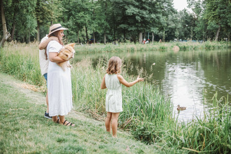 Family vacation . Unrecognizable dad, mom and daughter are feeding ducks on shore of forest lake.の写真素材