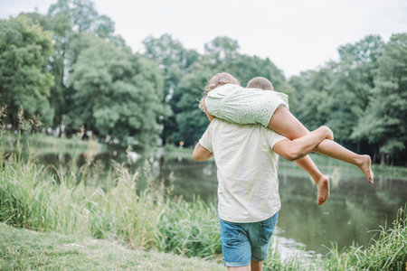 Unrecognizable father and daughter enjoy walk in nature , dad carries his daughter on his shoulder.の写真素材