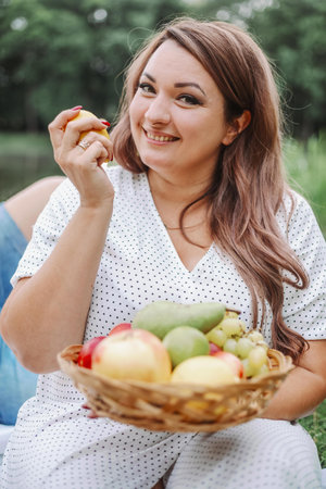 Vertical portrait of charming woman in light dress holding plate of fruit at summer picnic.の写真素材
