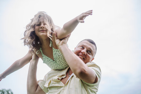 Happy childhood. Happy girl with flowing hair depicts flight hanging on Dads shoulder. Fatherhood.の写真素材