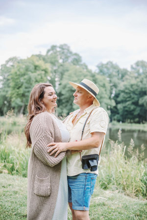 Beautiful smiling brown - haired woman inlong knitted cozy cardigan hugs her husband on summer.の写真素材