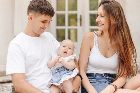 Smiling married couple with little daughter is sitting on summer day against background of house.の写真素材