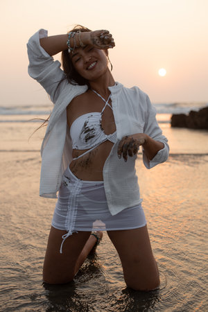 Portrait of young satisfied Asian pretty woman wearing wet dirty white swimsuit, shirt skirt standing on knees in water.の写真素材