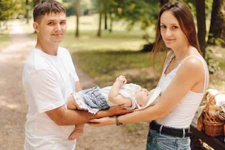 Protection, protection of childhood. Happy parents with their baby on summer day for walk in park.の写真素材
